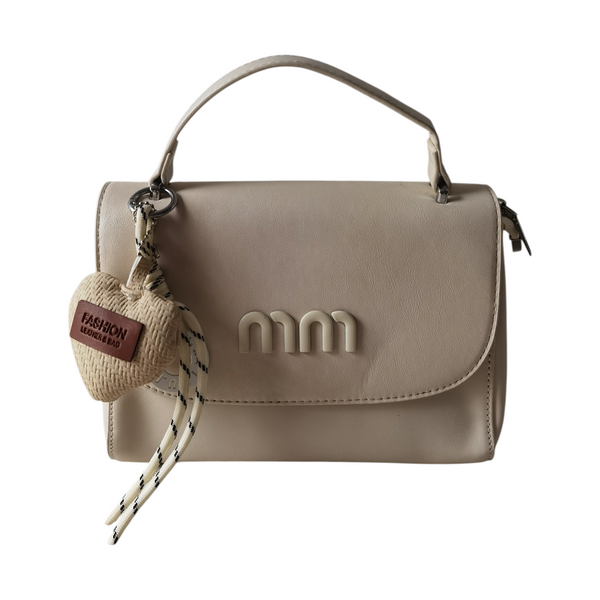 Cartera ZEFORA Mía color crema, diseño compacto con solapa, asa superior y charm decorativo en forma de corazón.