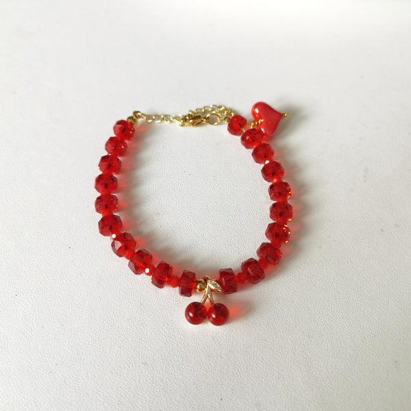 Descubre la pulsera Cherry con cuentas rojas, detalles dorados y dije de cerezas. Largo 16.5 cm más cadena de extensión de 5 cm. Ideal para un look femenino y moderno.