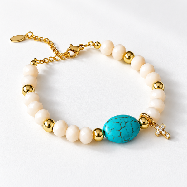Descubre la pulsera Turquesa Celeste con cuentas color crema, piedra central turquesa y dije de cruz dorada. Un accesorio femenino y elegante